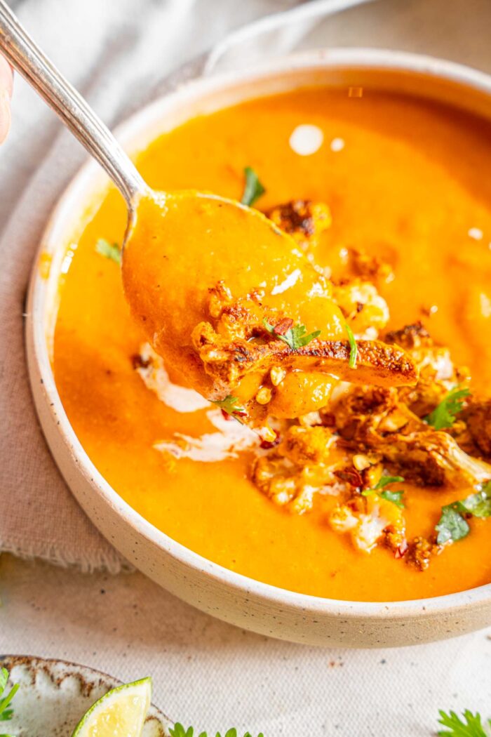 A spoonful of sweet potato cauliflower soup lifted out of the bowl (close up).