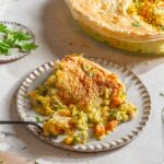 Veggie pot pie served on a plate, with the rest of the pie in a pan in the background.