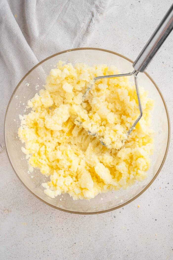 Boiled potatoes mashed in a glass bowl.