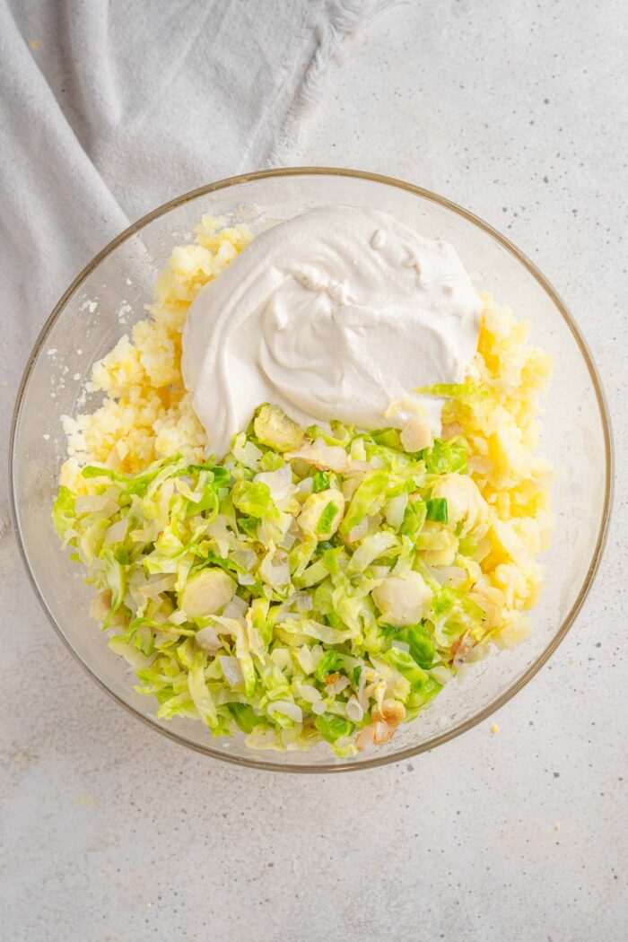 Potatoes, Brussels sprouts, onions, and cashew cream in a glass bowl.