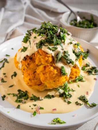 Title image: whole roasted cauliflower with tahini and herb salsa on a white platter.