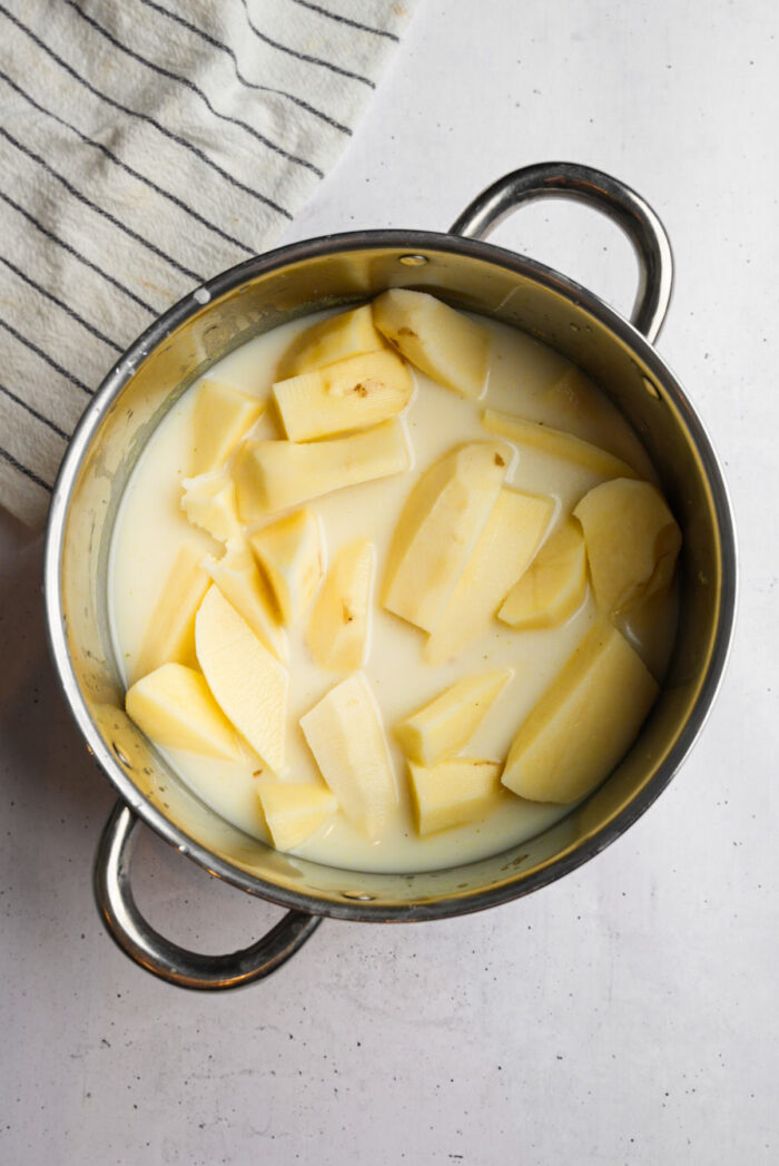Potatoes in a steel pot with vegetable broth and plant-based milk.