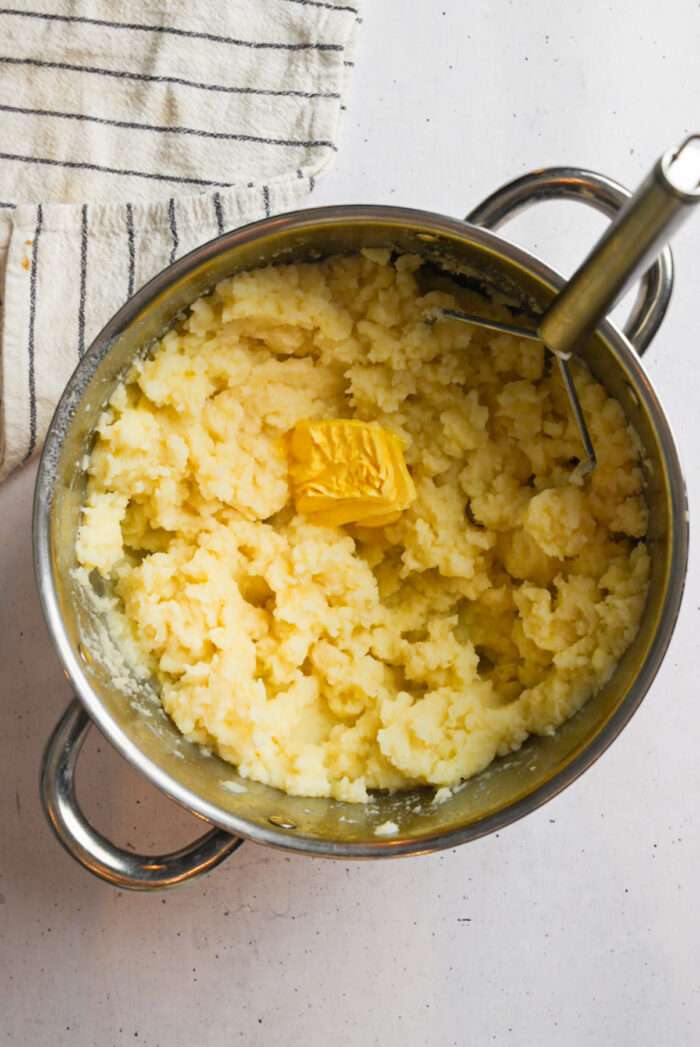 A blob of vegan butter added to mashed potatoes in a steel pot.