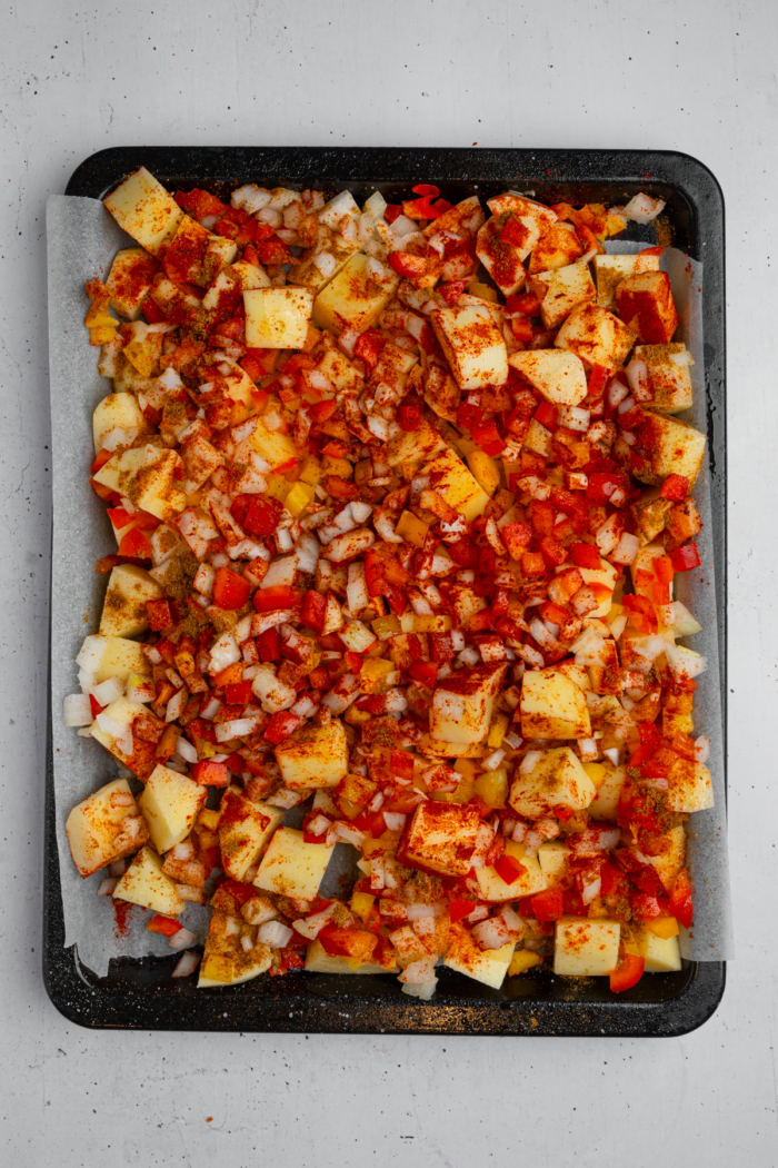 Potatoes, bell peppers, onions and seasonings laid out on a baking sheet.