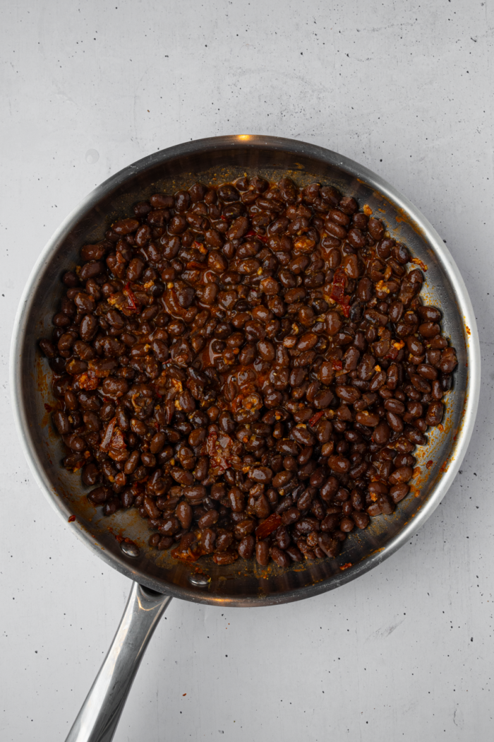 Canned black beans in a frying pan with garlic and seasonings.