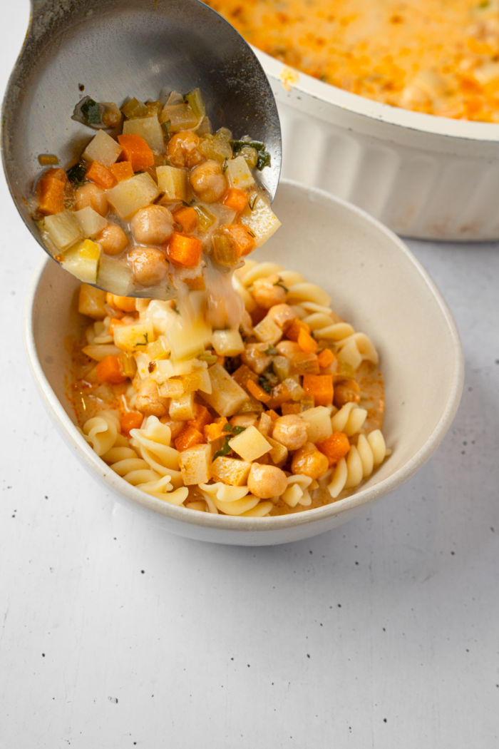 Creamy vegetable soup being poured over cooked noodles.
