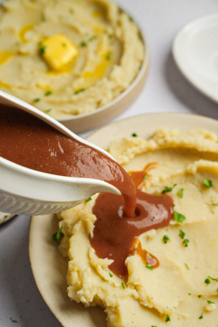 Vegan mashed potatoes with brown gravy being poured over the top.