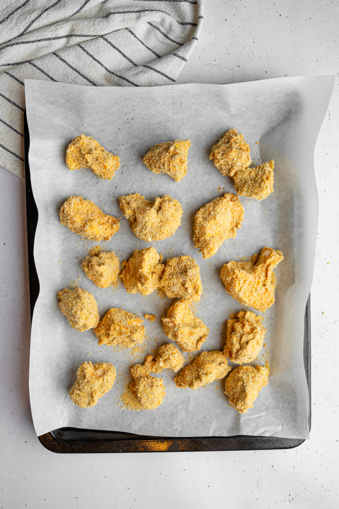 Cauliflower coated in breadcrumbs and laid out on a lined sheet pan.