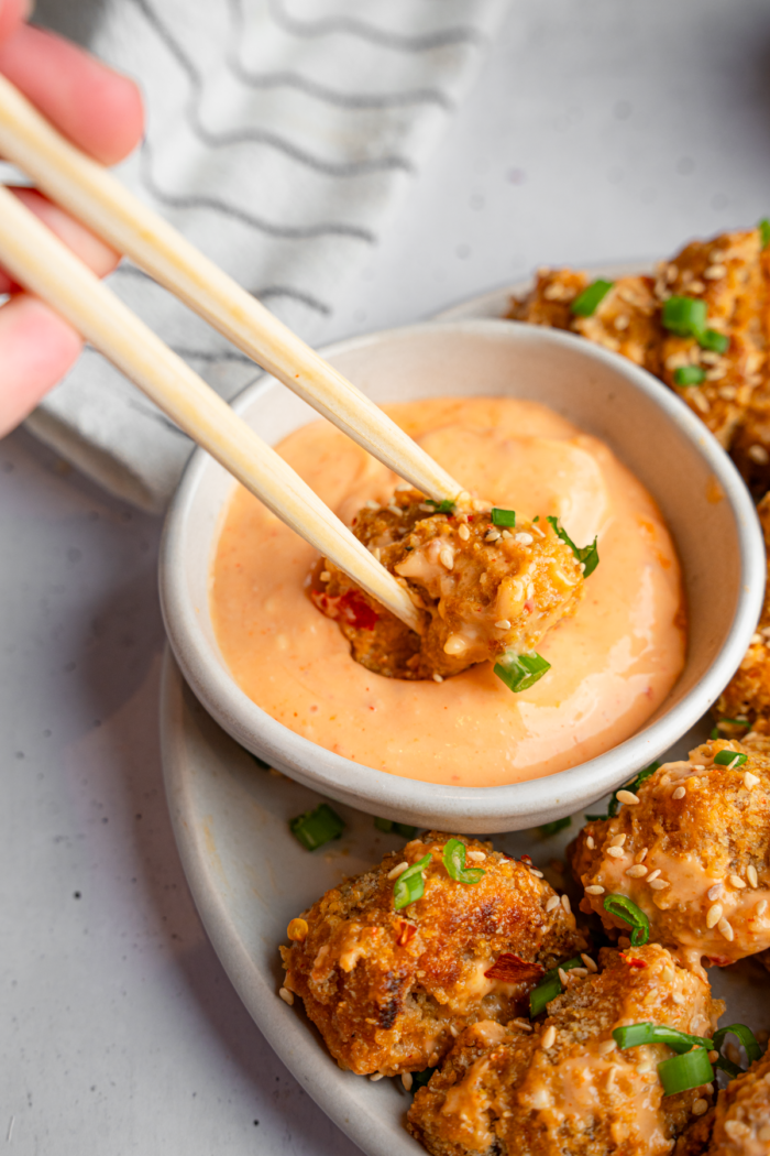 Bang bang cauliflower being dipped in sauce using chopsticks.