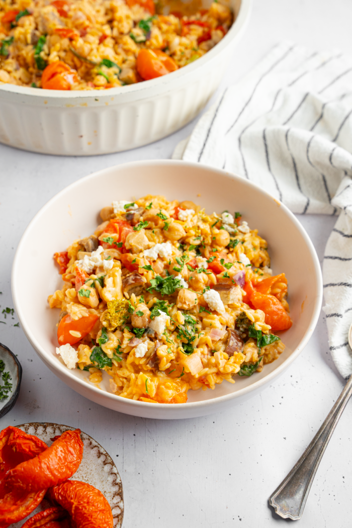A serving of baked orzo with veggies in a white ceramic bowl.