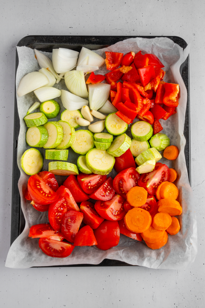 Vegetables arranged on a lined baking sheet with some avocado oil.