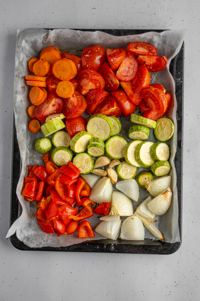 Chopped roasted vegetables on a lined baking sheet, fresh out of the oven.