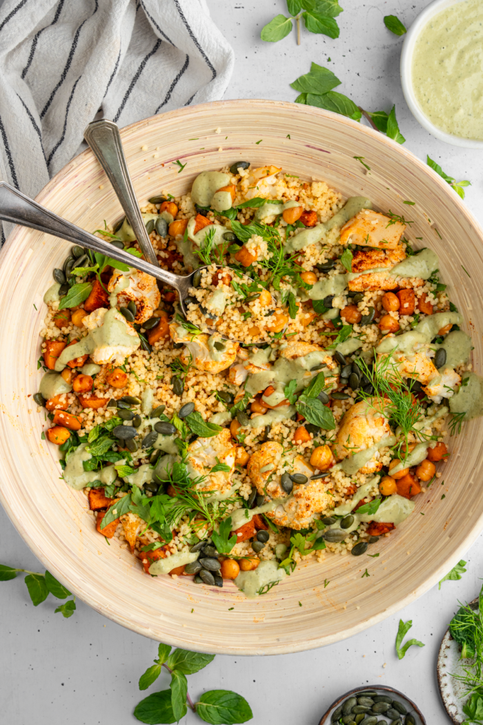 Top down shot of a salad bowl filled with vibrant sweet potato and cauliflower herb couscous salad.