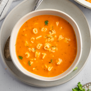 Top down shot of the healthy alphabet soup served in a ceramic bowl with some fresh herbs.
