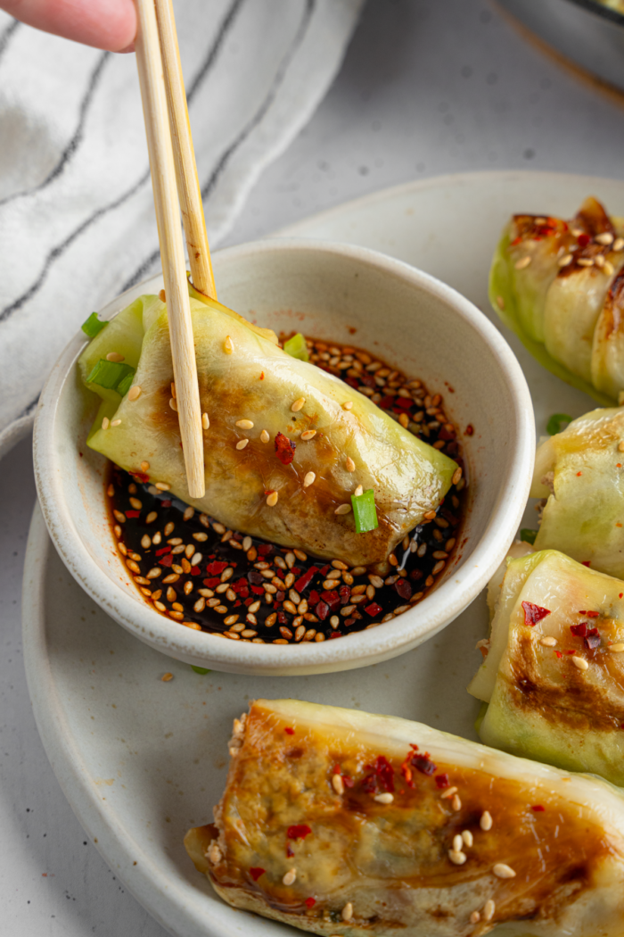 Chopsticks dipping a cabbage roll in sauce.