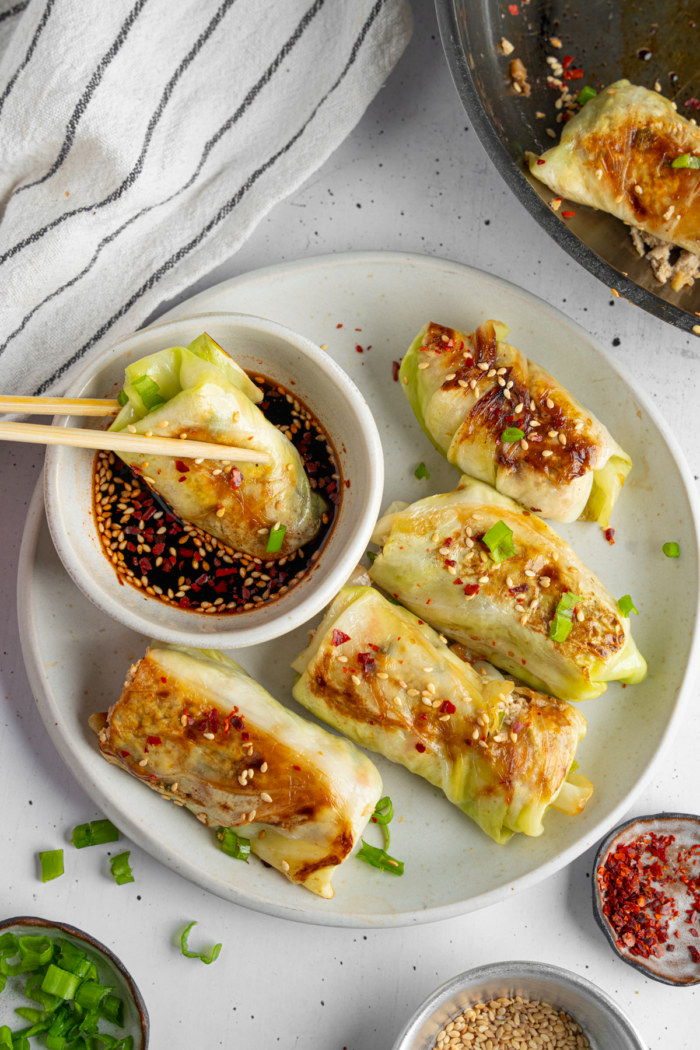 Top down view of a plate of vegan cabbage wrapped dumplings, with chopsticks dipping one dumpling in sauce.