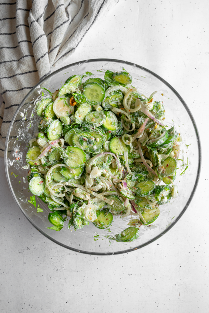 The vegan creamy cucumber salad mixed together in a glass salad bowl.