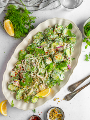 Title image of vegan creamy cucumber salad served on a large oval platter with the garnish of dill and lemon.