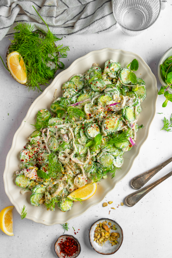 Title image of vegan creamy cucumber salad served on a large oval platter with the garnish of dill and lemon.
