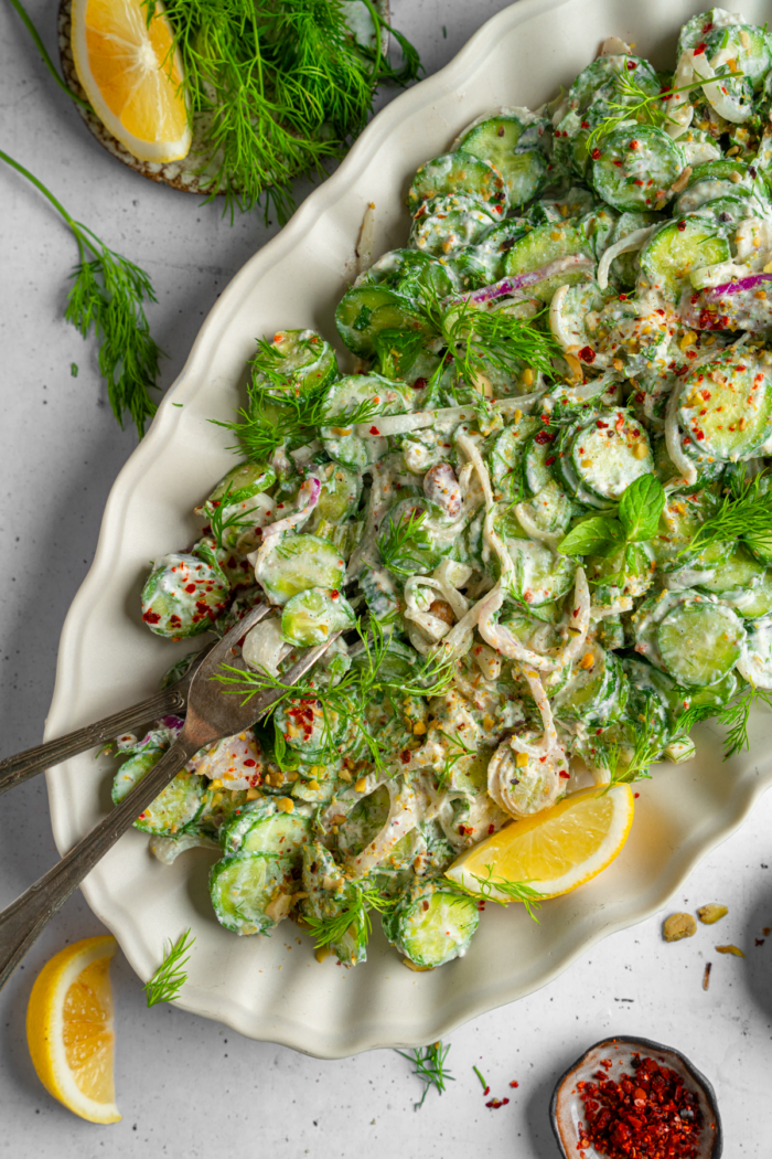 Top down shot of vegan creamy cucumber salad with serving utensils and garnish.