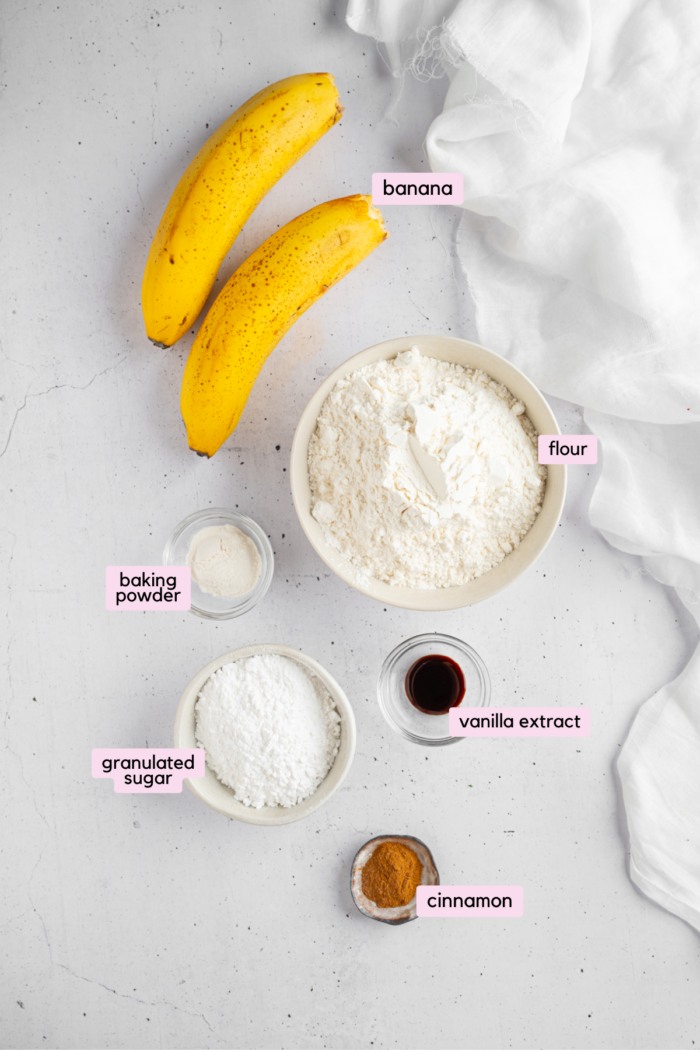 Ingredients for banana donut holes laid out and labeled on a light background.