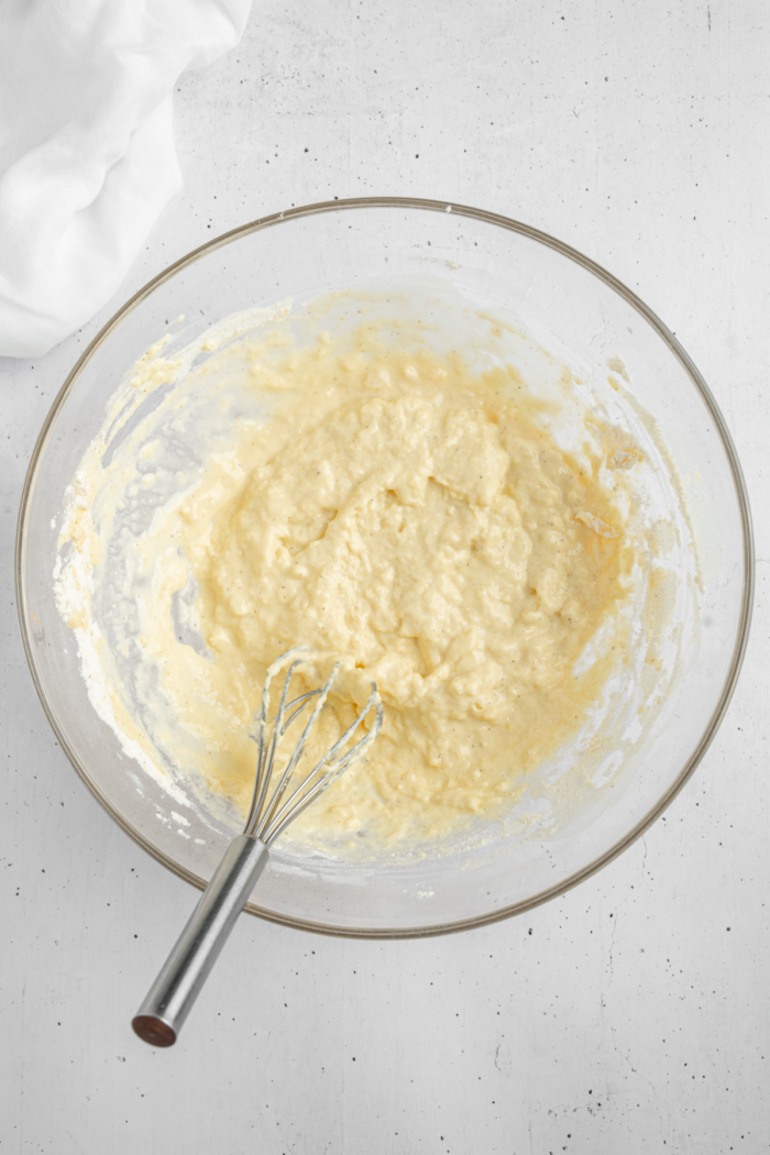 Thick pancake batter in a glass bowl with a whisk sticking out.