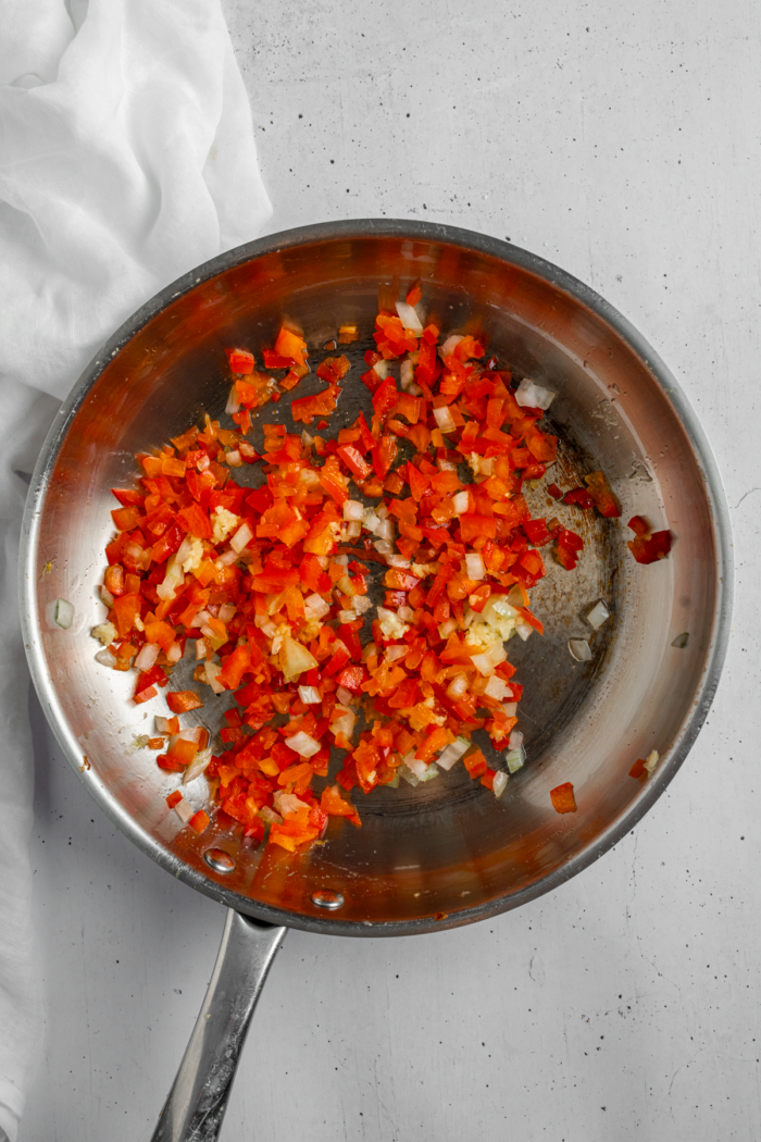 Onion, garlic, and bell pepper cooking in a steel frying pan with olive oil.
