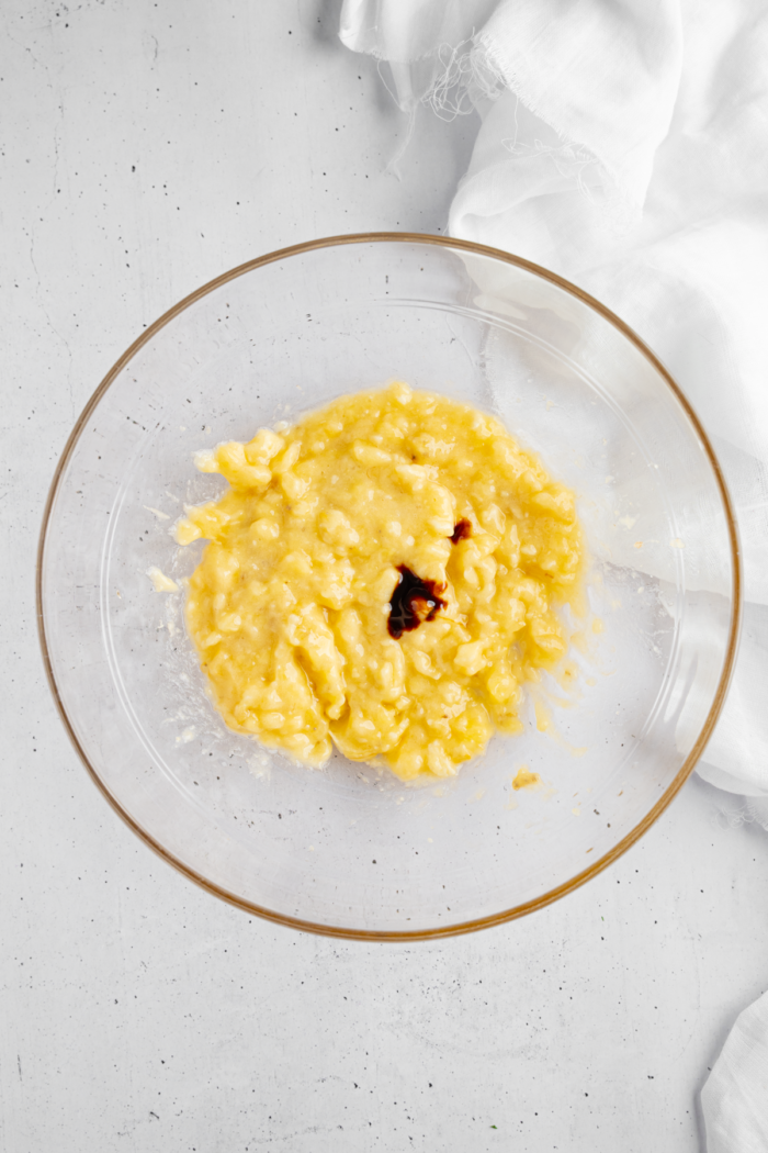 Mashed bananas and vanilla extract in a glass bowl.