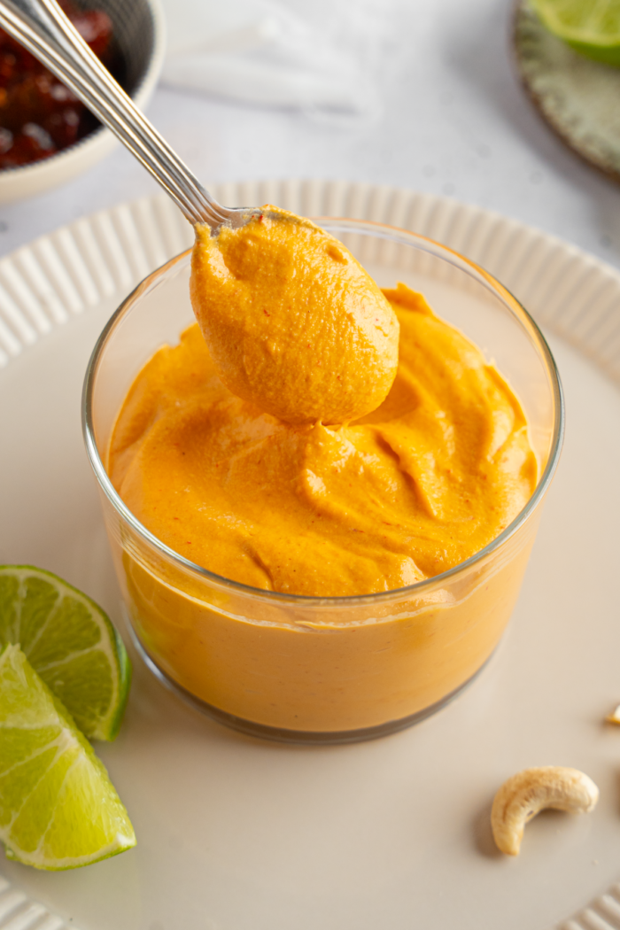 Vegan chipotle mayo in a glass cup, with a spoonful of mayo lifted out.