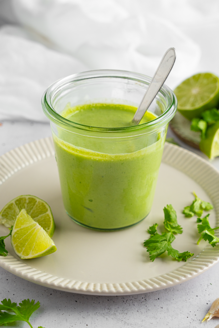 Vegan Cilantro Lime Dressing in a glass jar, garnished with greens and lime.