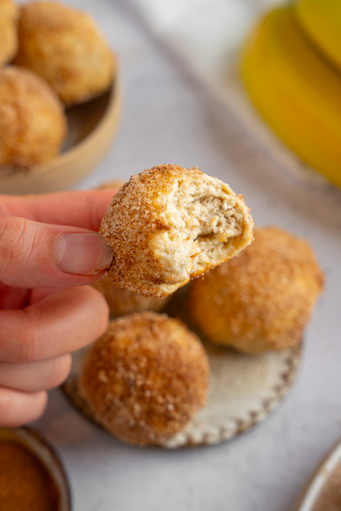 A banana donut hole with a bit taken out held up to the camera.