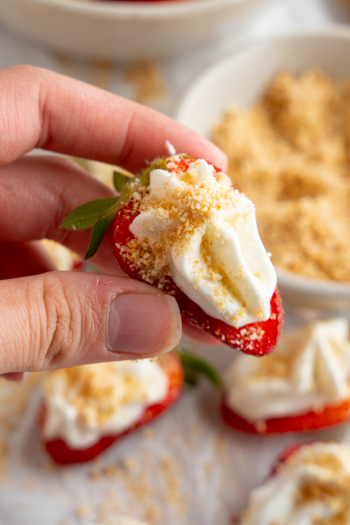A close up of a woman's hand holding a deviled strawberry topped with graham cracker crumbs.