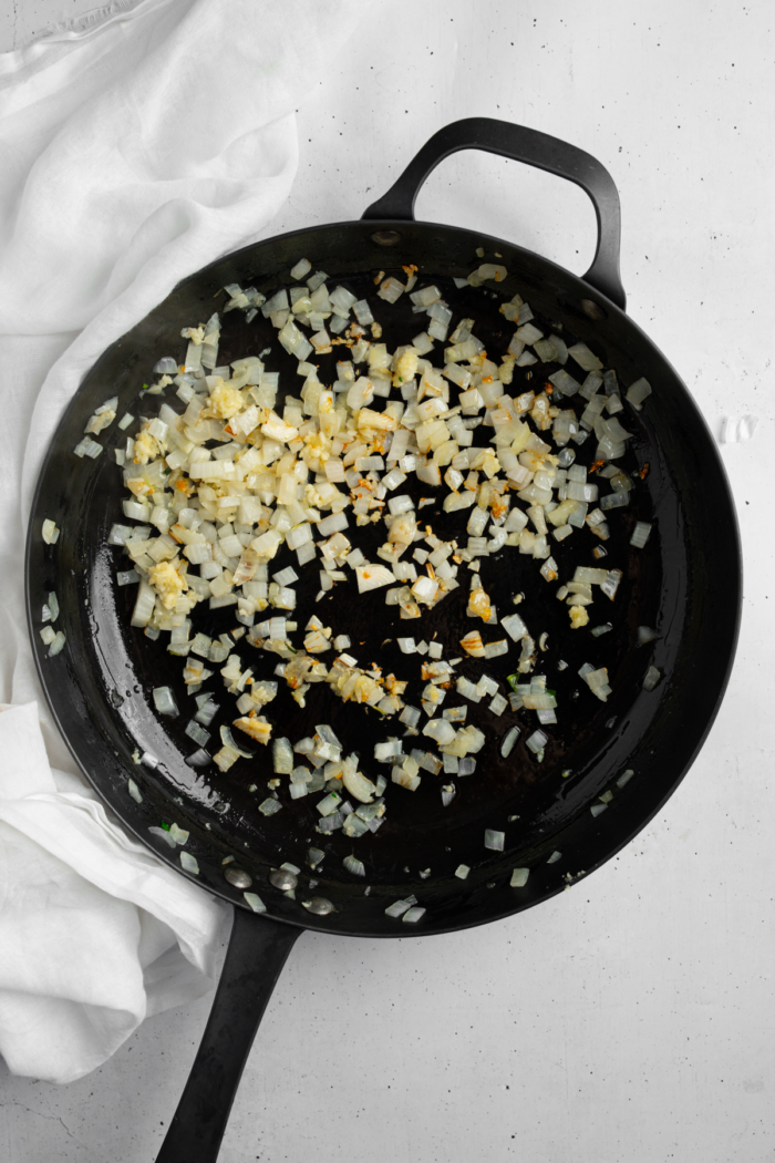 Garlic and onion being sauteed in a cast iron pan.