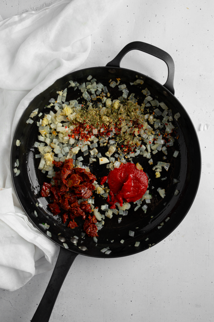 Sundried tomatoes, tomato paste, and seasoning added to the pan with sauteed garlic and onion.