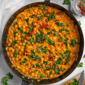 Title image: marry me chickpeas in a large cast iron pan with ingredients and garnish visible in the background.