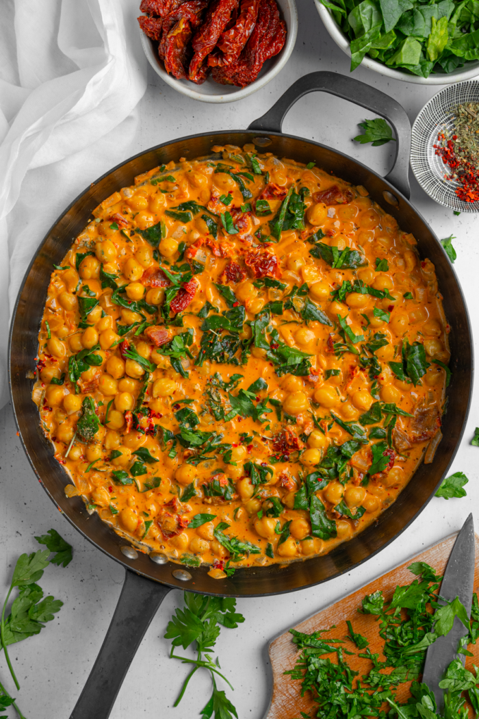Title image: marry me chickpeas in a large cast iron pan with ingredients and garnish visible in the background.