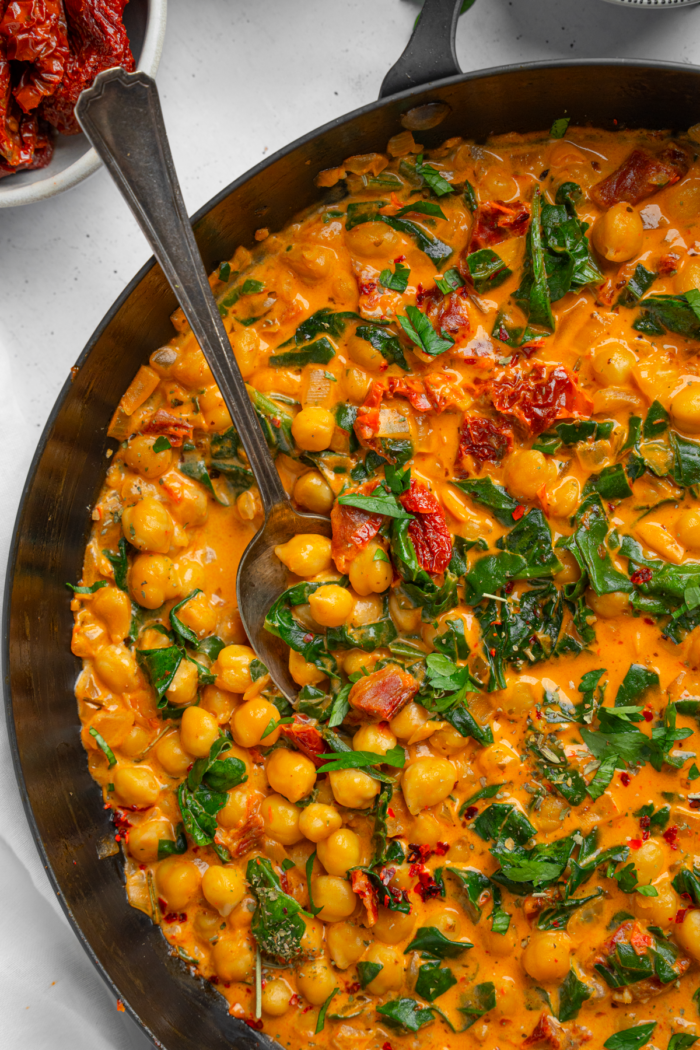 A spoon sticking out of the creamy and thick marry me chickpeas pan.