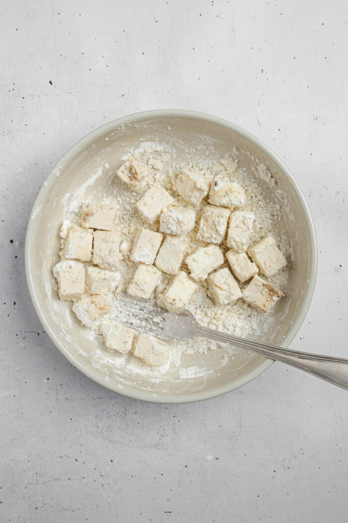A shallow bowl of cornstarch, with tofu cubes being dipped into it.