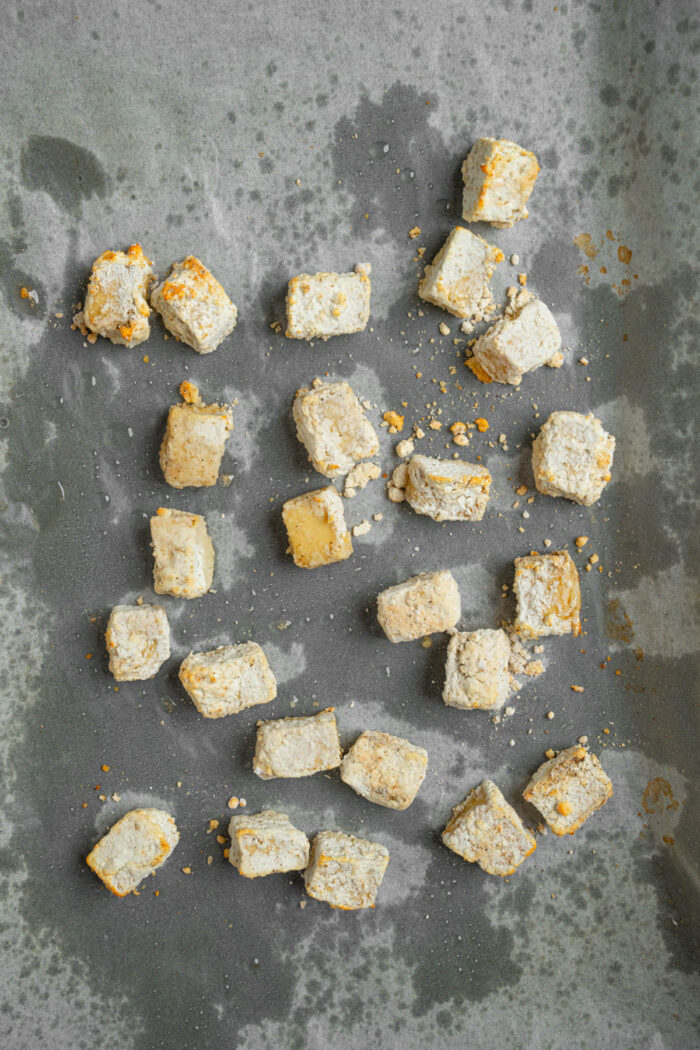 Baked crispy tofu cubes on a lined baking sheet.