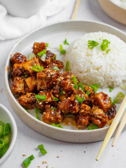 Vegan "honey" garlic tofu served with steamed or boiled rice and greens for garnish.