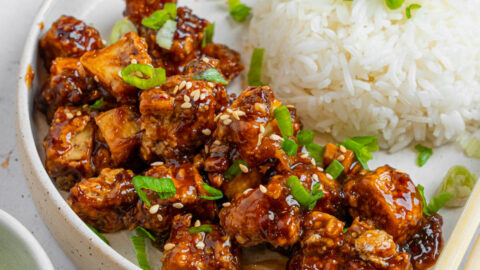 Vegan "honey" garlic tofu served with steamed or boiled rice and greens for garnish.