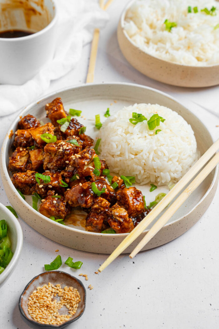Vegan "honey" garlic tofu served with rice, sesame seeds, and fresh herbs.