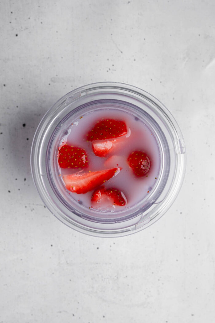Frozen strawberries with other ingredients for homemade electrolyte drink in a high-speed blender.