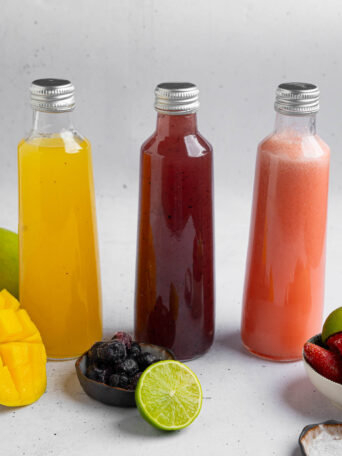 Homemade electrolyte drinks flavored with strawberry, blueberry, and mango, served in glass bottles.