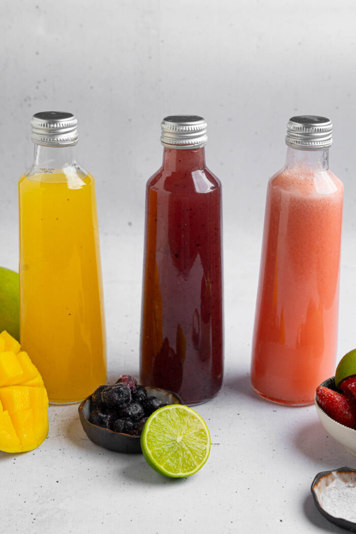 Homemade electrolyte drinks flavored with strawberry, blueberry, and mango, served in glass bottles.