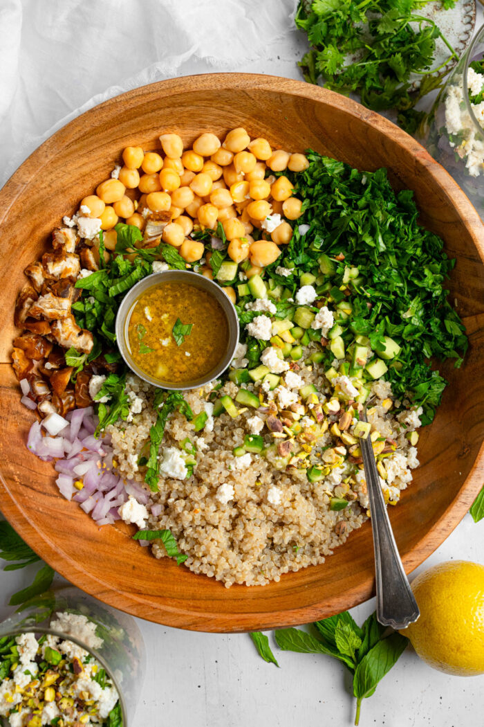 A large salad bowl with vegan couscous salad ingredients and dressing.