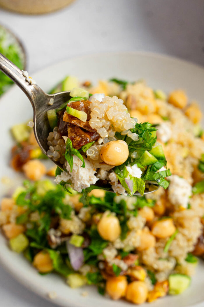 A spoonful of Vegan couscous salad with feta and mint at the forefront, with the rest of the salad visible behind it.