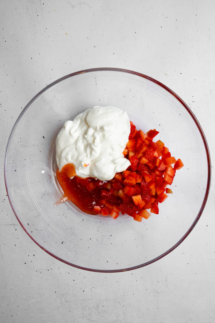 The ingredients for strawberry yogurt mixture added to a glass bowl.