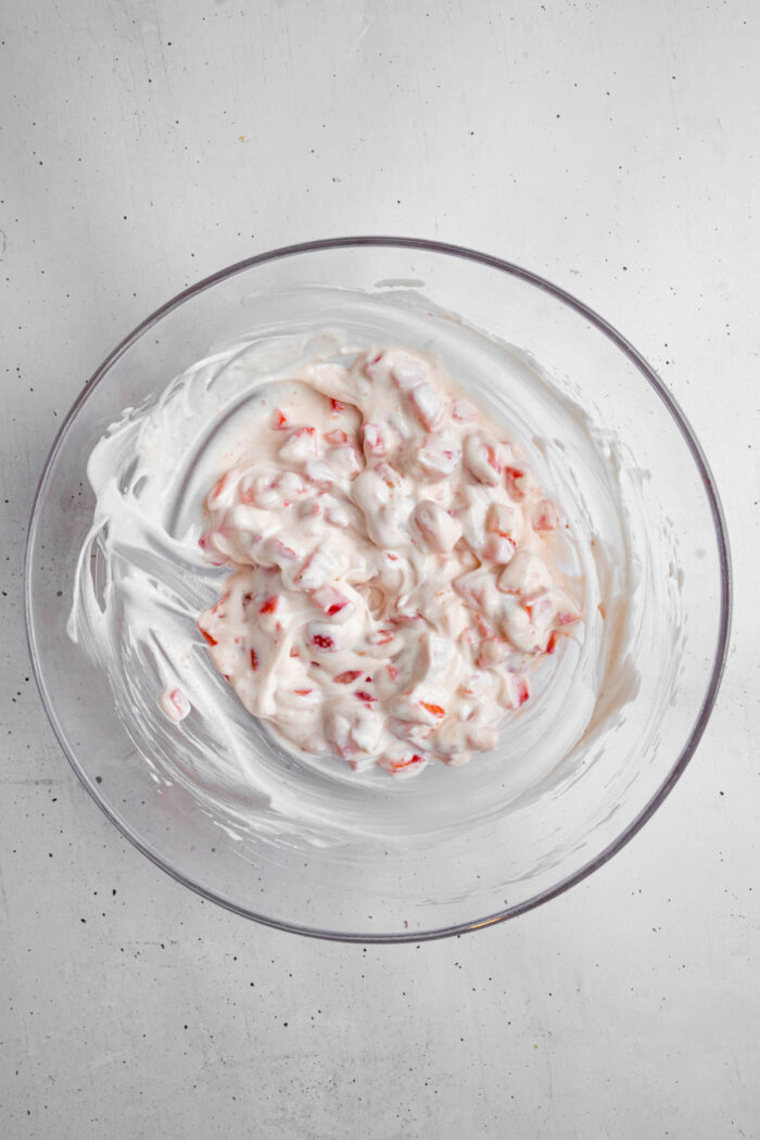 The mixture of yogurt, strawberries and jam in a glass bowl.