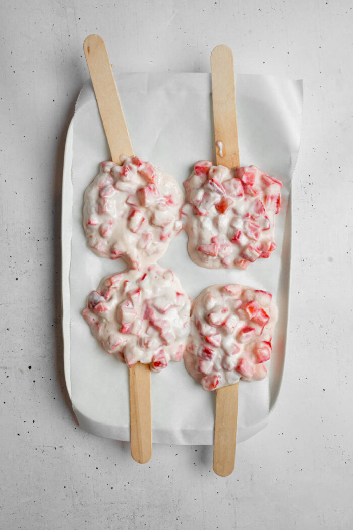 Newly formed strawberry clusters on a lined baking tray, with popsicle sticks.
